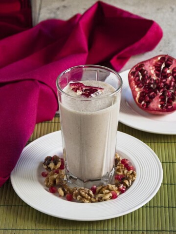 Pomegranate Smoothie with Banana and Walnuts in a glass surrounded by pomegranate and walnuts