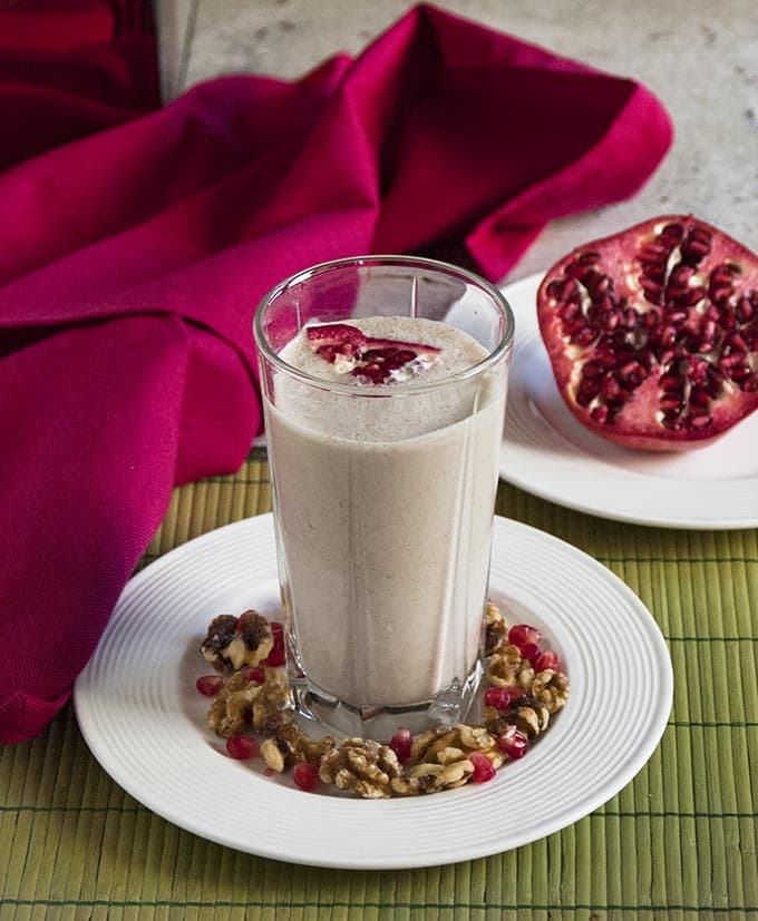 Pomegranate Smoothie with Banana and Walnuts in a glass surrounded by pomegranate and walnuts