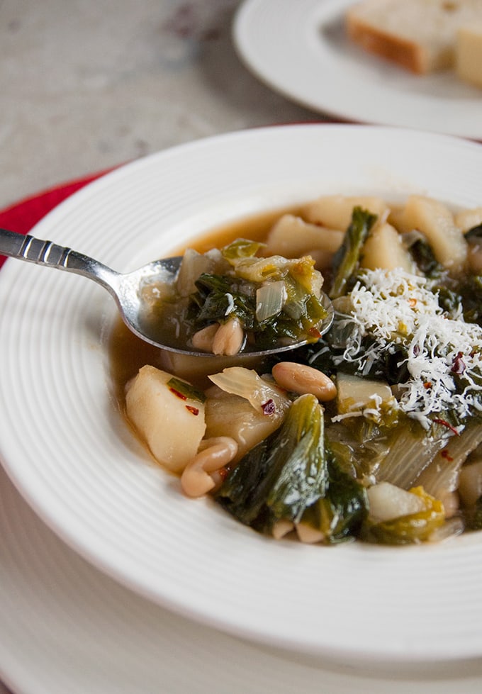 spoonful of Tuscan white bean soup with escarole and potatoes being taken from the bowl