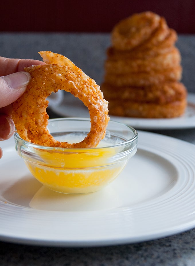 baked parmesan gluten-free onion ring being dipped in melted butter