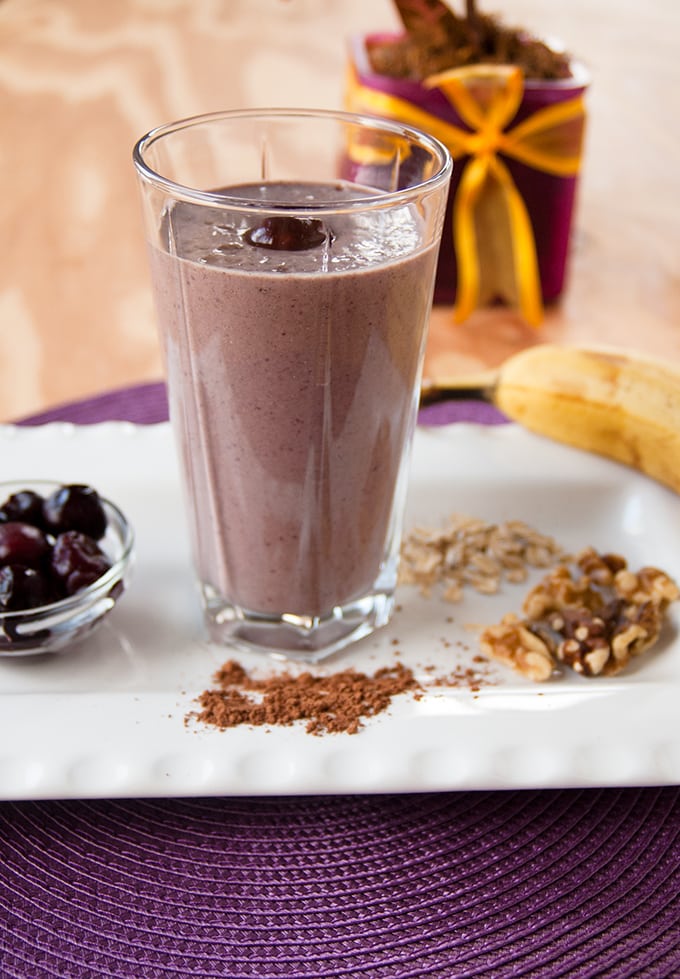 Chocolate-Covered Cherry-Almond Smoothie on a platter with banana, oats, walnuts, cocoa and cherries