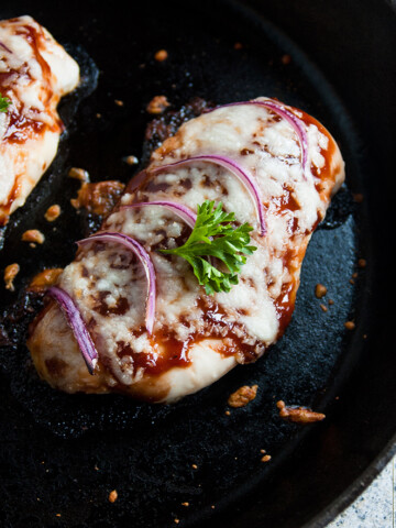 overhead view of cheesy baked BBQ chicken breasts in a skillet