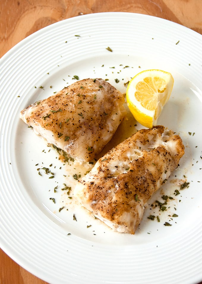 overhead view of two pieces of Baked Cod with Coffee Butter on a plate with a lemon wedge