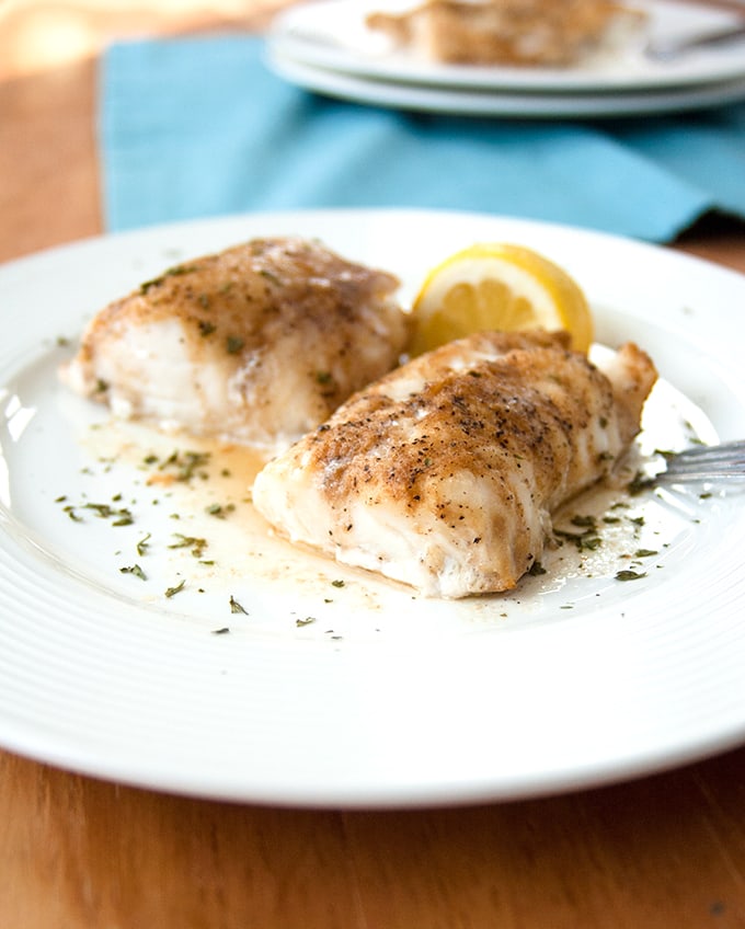 two pieces of Baked Cod with Coffee Butter on a plate with lemon and fork