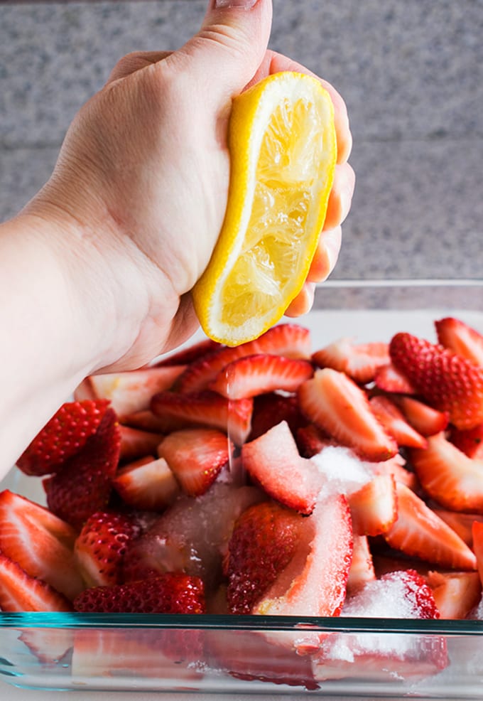 hand squeezing lemon juice onto strawberries and sugar
