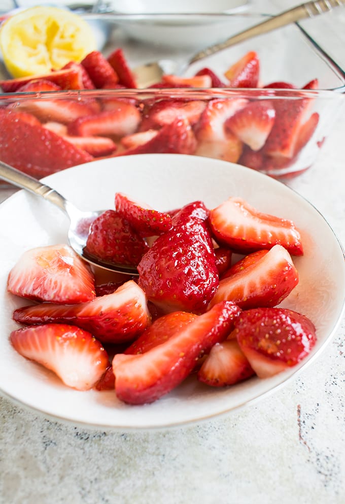 Italian Strawberries with Sugar and Lemon in a bowl with a spoon, pan of Strawberries with Sugar and Lemon behind the bowl