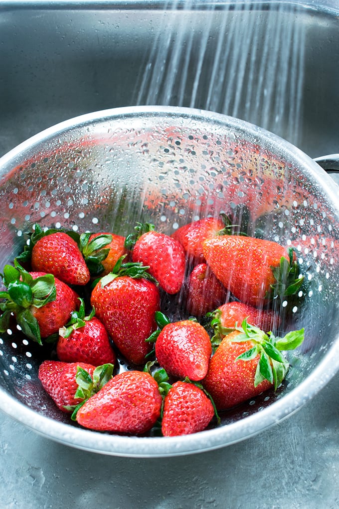 strawberries being rinsed in a colander 
