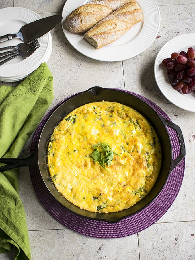 spread of baked arugula frittata, a bunch of grapes and loaf of bread with forks and knives