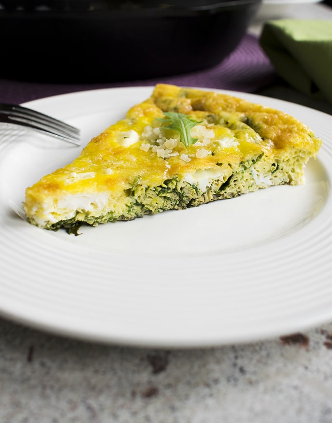 slice of baked arugula frittata on a plate with a fork