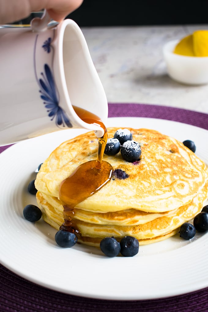 maple syrup being poured on a stack of lemon-blueberry pancakes