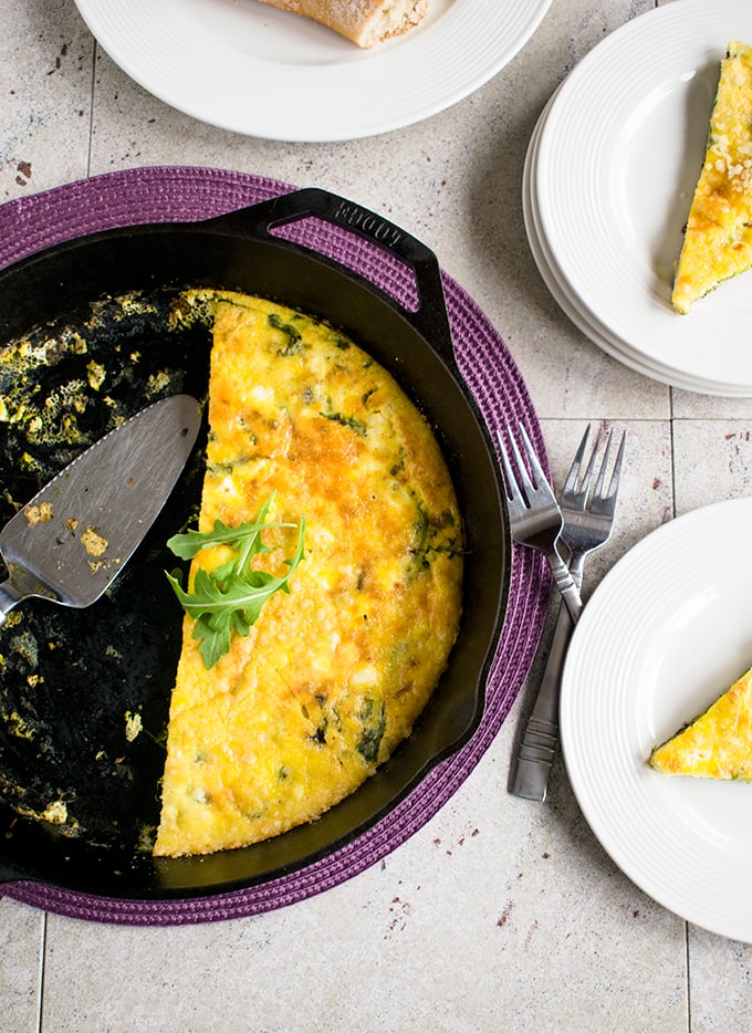 half of a baked arugula frittata in a skillet, slices of baked arugula frittata on plates beside it 