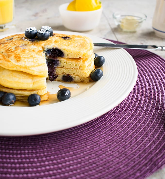 stack of lemon-blueberry pancakes with a wedge removed on a plate