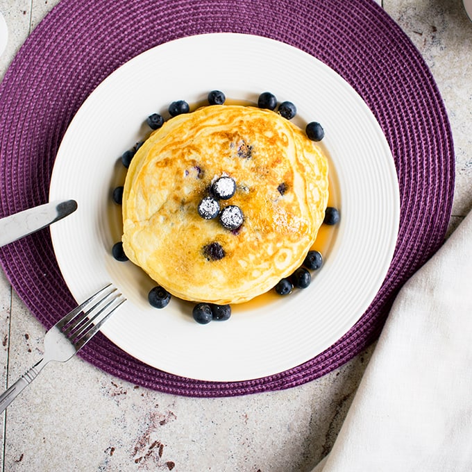 overhead view of lemon-blueberry pancakes on a plate with fork and knife