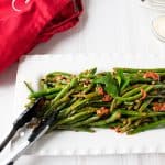 Italian green beans with tomatoes on a platter with tongs