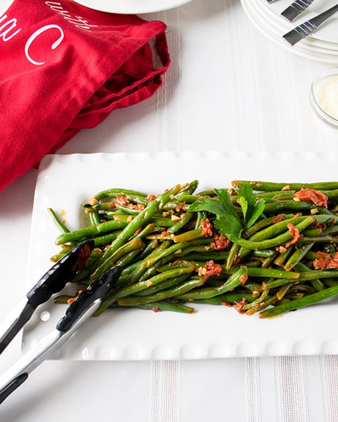 Italian green beans with tomatoes on a platter with tongs 