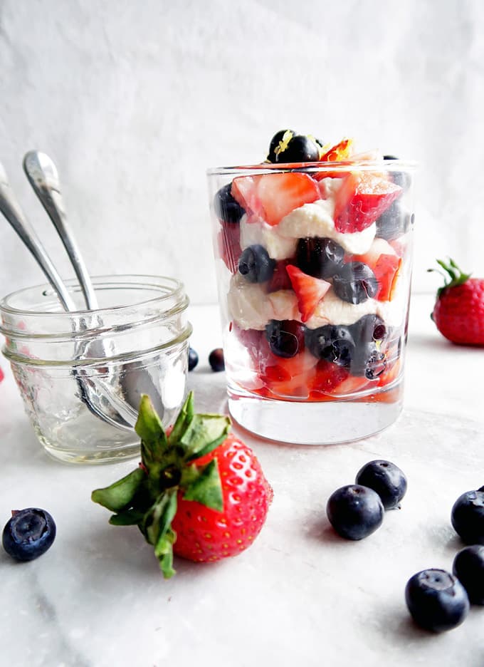 Glass of fresh berries with mascarpone cream and small mason jar with spoons, blueberries and strawberries 