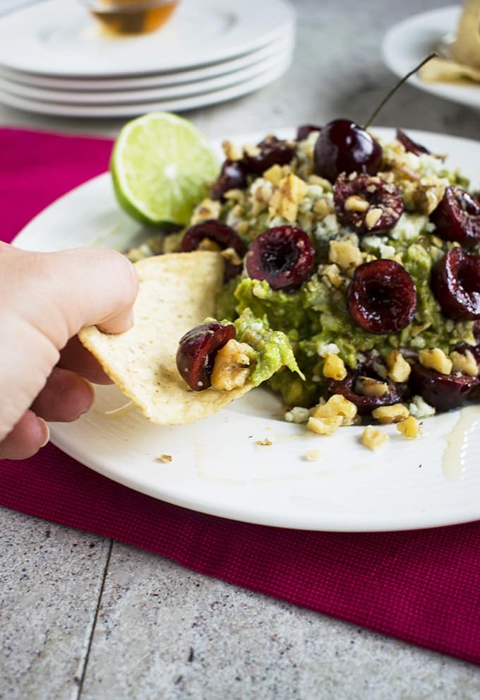 chip being dipped in guacamole with cherries, gorgonzola and walnuts