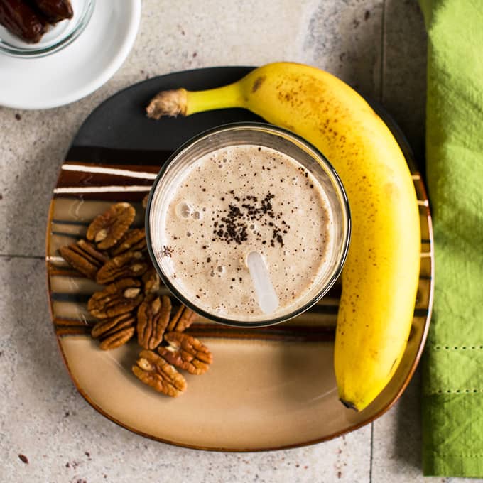 overhead view of glass of homemade vanilla frappuccino on a plate with bunch of pecans and banana