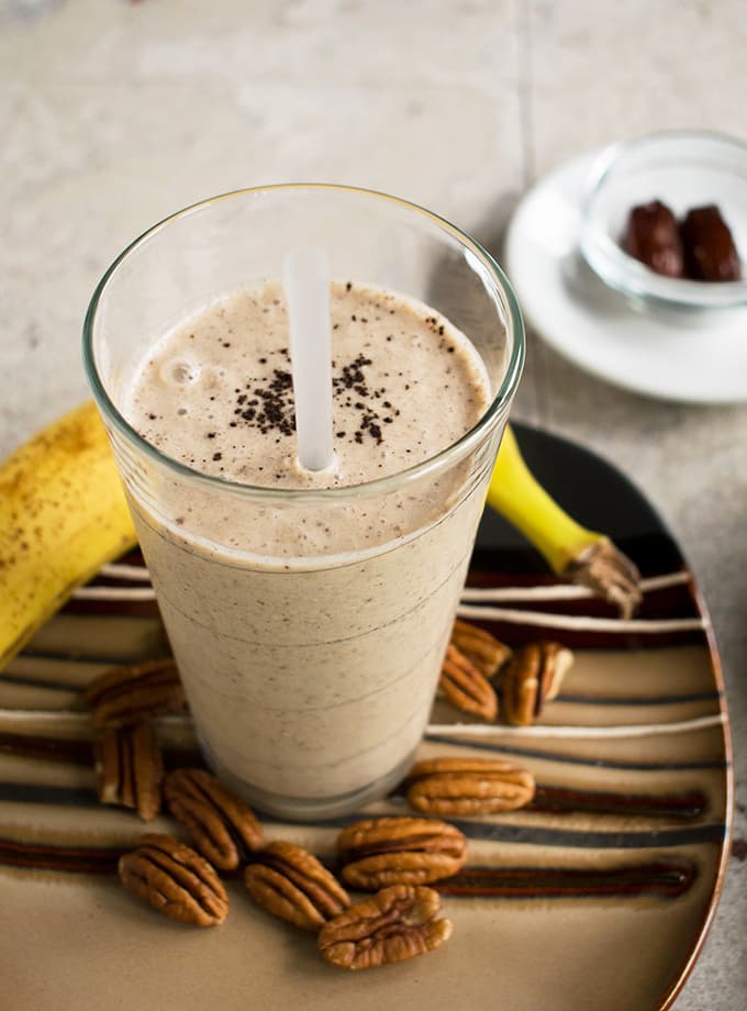 glass of healthy homemade vanilla frappuccino on a plate surrounded by pecans, banana