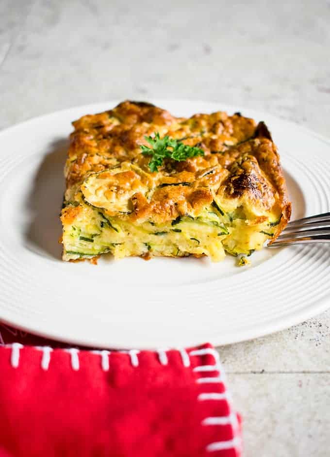 portion of zucchini casserole on a white plate with a fork and red napkin