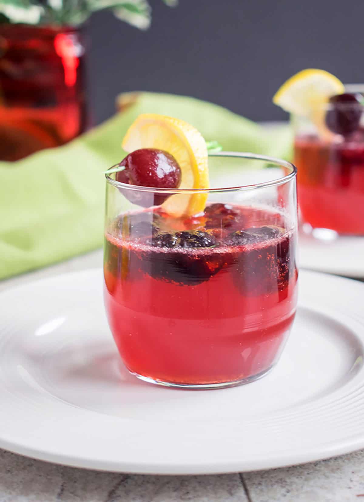 a glass of black cherry cocktail with a cherry and lemon
