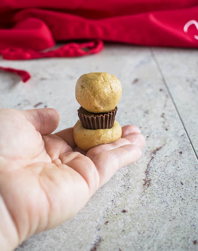 hand holding a peanut butter cup sandwiched by peanut butter cookie dough 