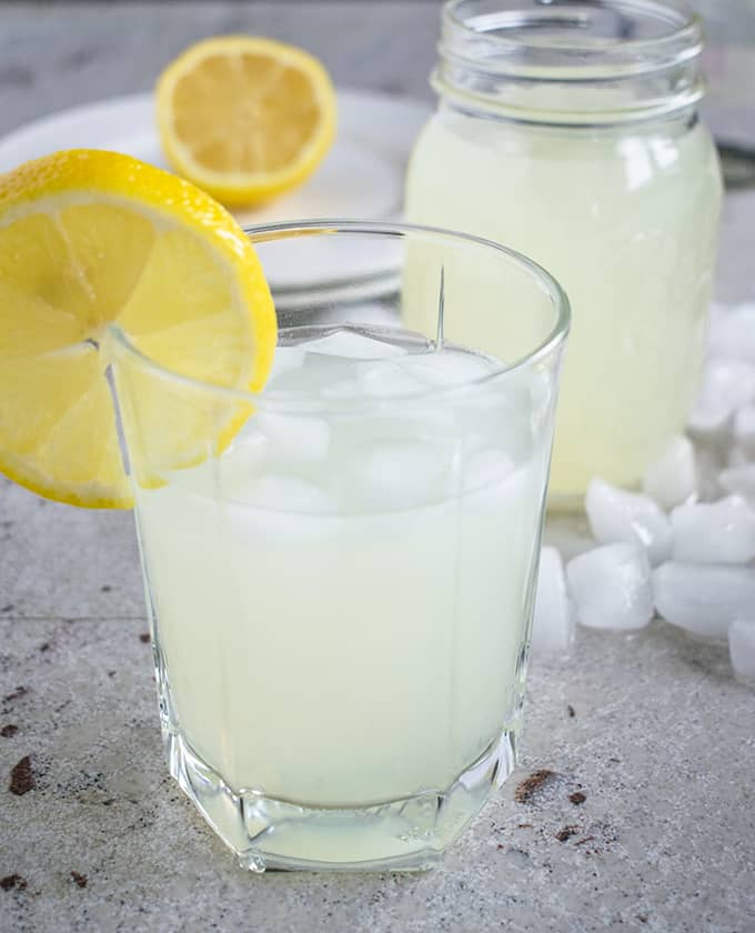 close up photo of lemonade moonshine in a glass in front of a jar 