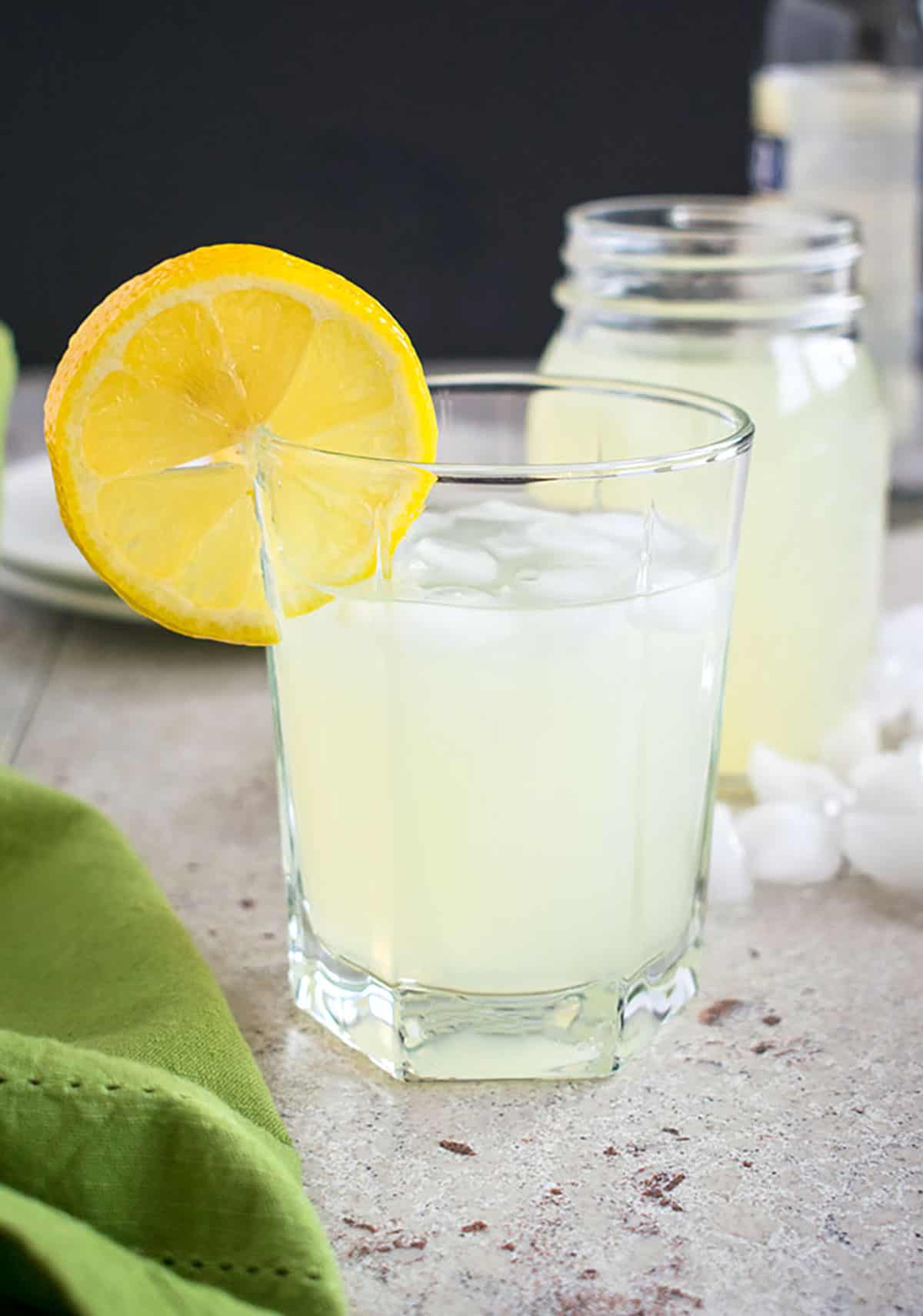 glass of lemonade moonshine with a lemon garnish in front of a jar of lemonade moonshine