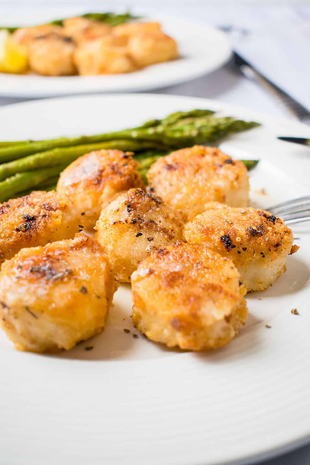 close-up photo of broiled scallops with parmesan bread crumbs in front of asparagus on a plate