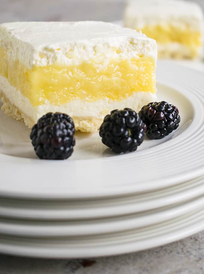 slice of lemon lush behind blackberries on stacked plates