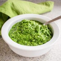 Photo of a white bowl filled with pesto, with a spoon dipped in and a napkin