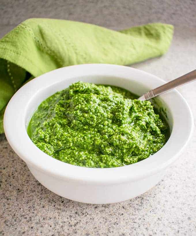 Photo of a white bowl filled with pesto, with a spoon dipped in and a napkin