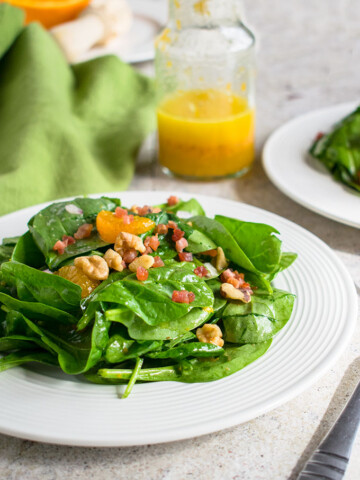 spinach salad topped with mandarin oranges and pancetta on a plate and a bottle of orange vinaigrette
