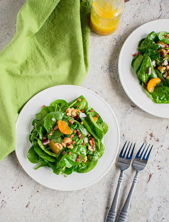 Overhead photo of two plates of Spinach Salad with Mandarin Oranges and Pancetta with two forks and green napkin