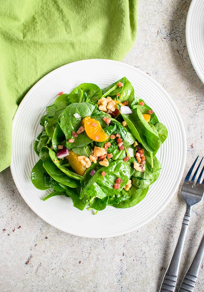 Plate of spinach salad with mandarin oranges and pancetta beside a fork and napkin