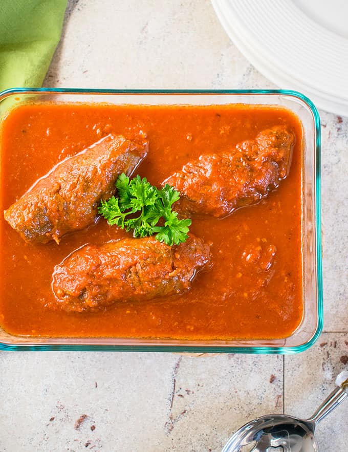 Overhead photo of three braciole in a glass container with sauce