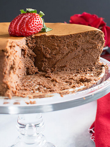 chocolate cheesecake on cake stand with sliced strawberry on top