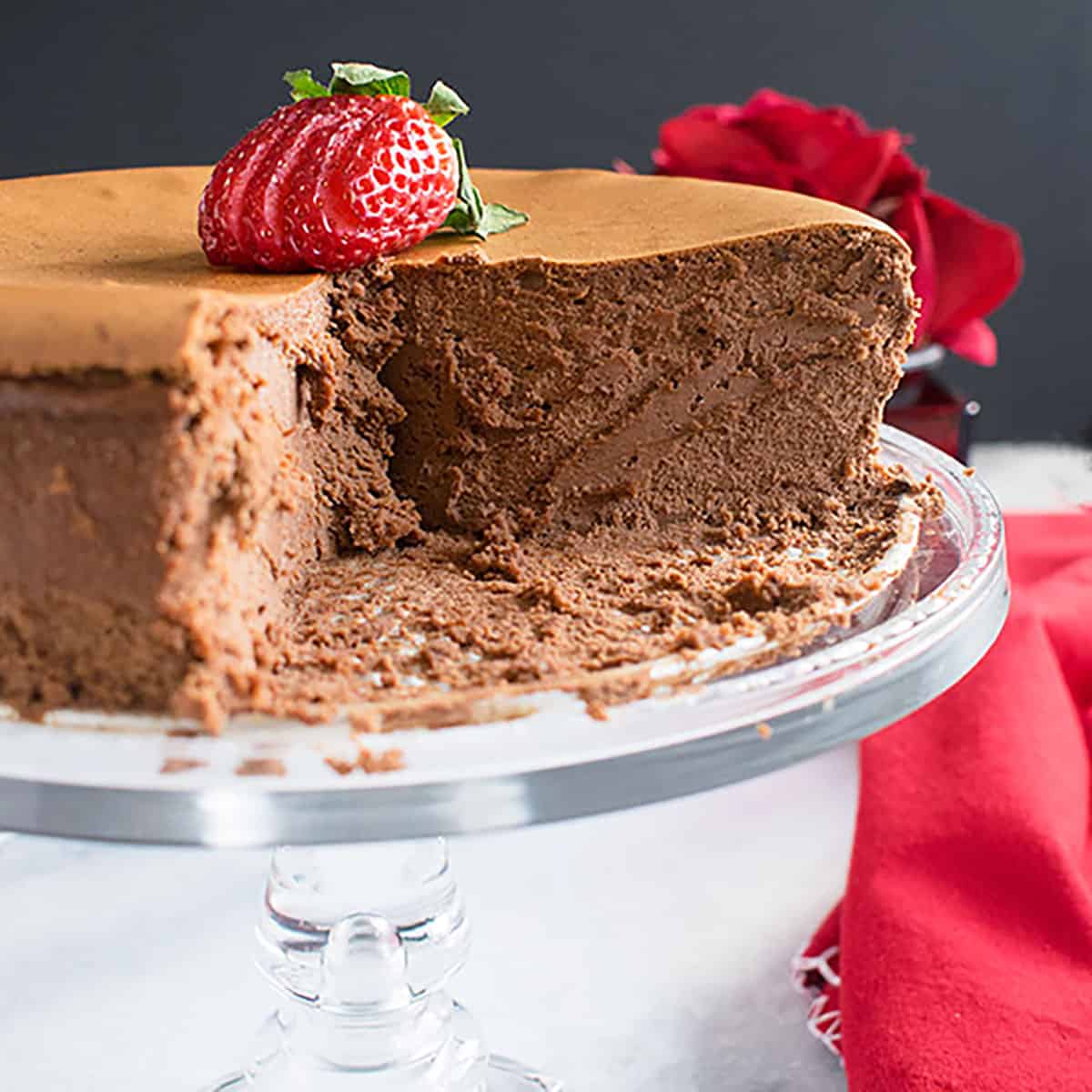 chocolate cheesecake on cake stand with sliced strawberry on top