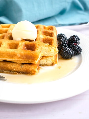 two stacked homemade waffles with butter, syrup and blackberries on a plate