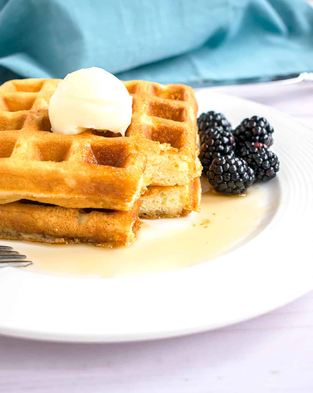 two stacked homemade waffles with butter, syrup and blackberries on a plate