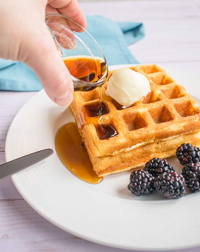 hand pouring maple syrup onto homemade waffles with blackberries