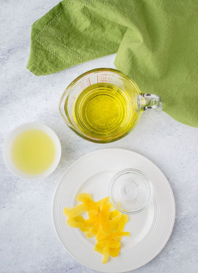overhead photo of a cup of olive oil, lemon juice, lemon peels and salt beside a green napkin