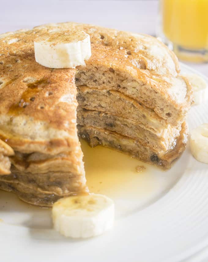 Stack of banana pancakes with a slice cut out and banana slices on a plate