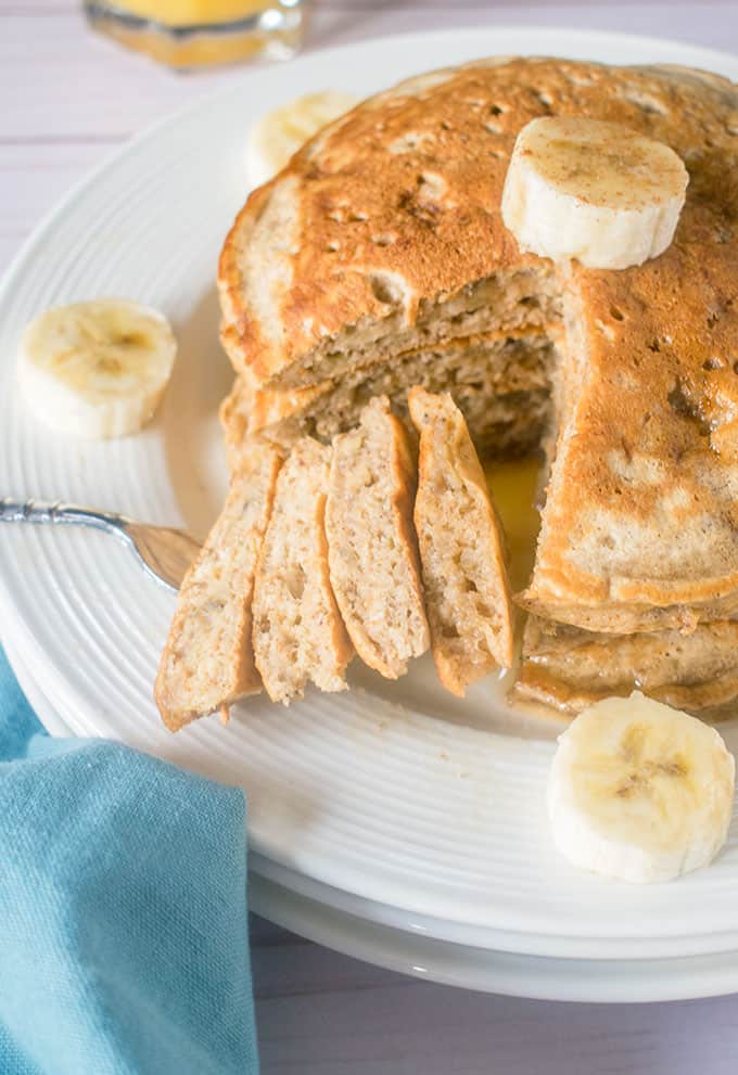 Stacked banana pancakes on a plate with a forkful taken out and banana slices 