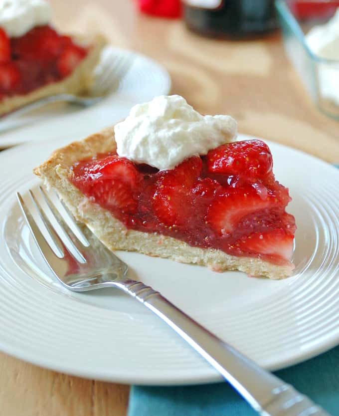 A slice of fresh strawberry pie with whipped cream and a fork on a plate