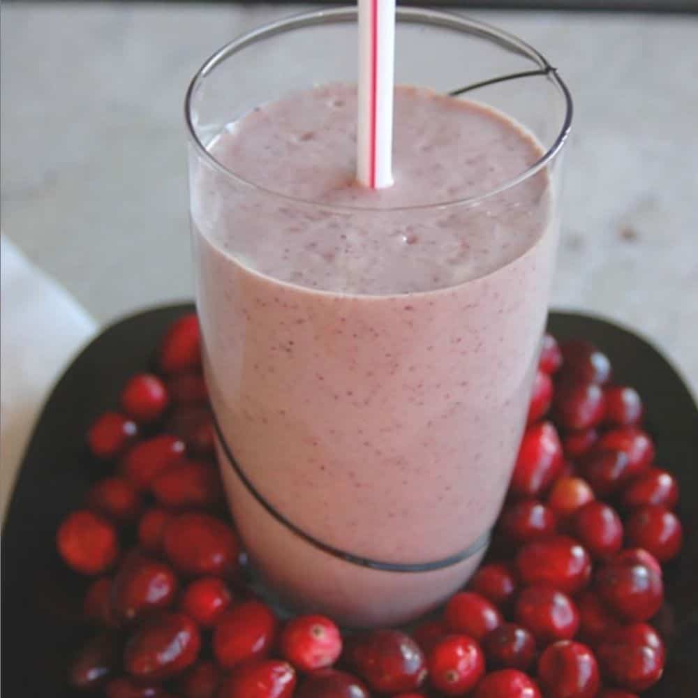 pink smoothie in glass in a bowl of cranberries