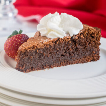 slice of chocolate cake with whipped cream and a strawberry on a stack of white plates, red napkin