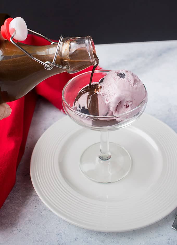 pouring chocolate liqueur over pink ice cream in a stemmed glass