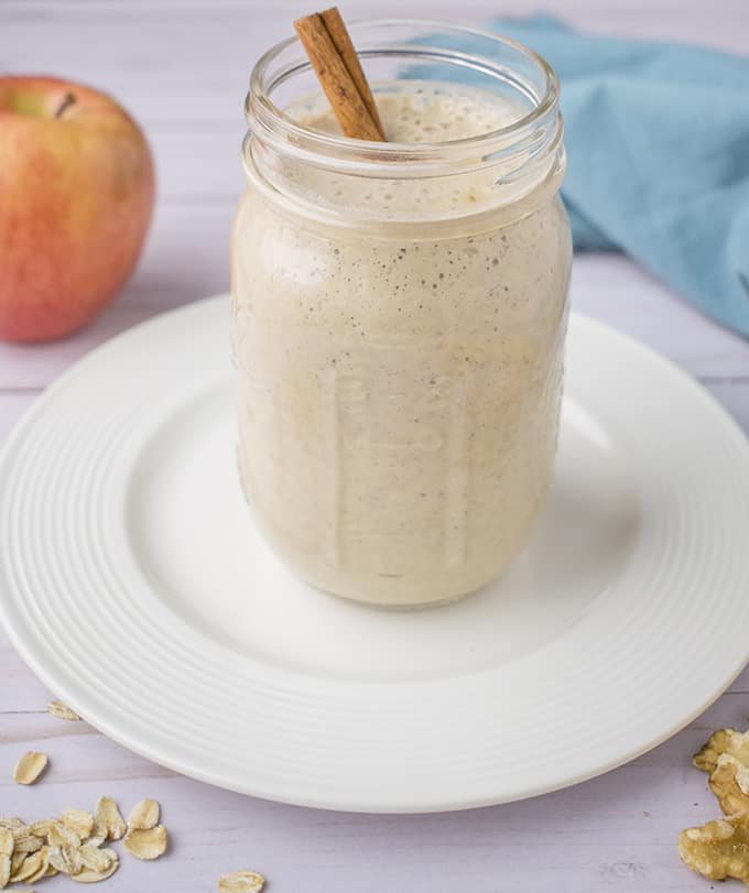 Einmachglas mit Apfel-Smoothie auf weißem Teller, roter Apfel, blaue Serviette