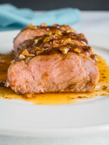 slices of glazed tenderloin on white plate with juices and blue napkin